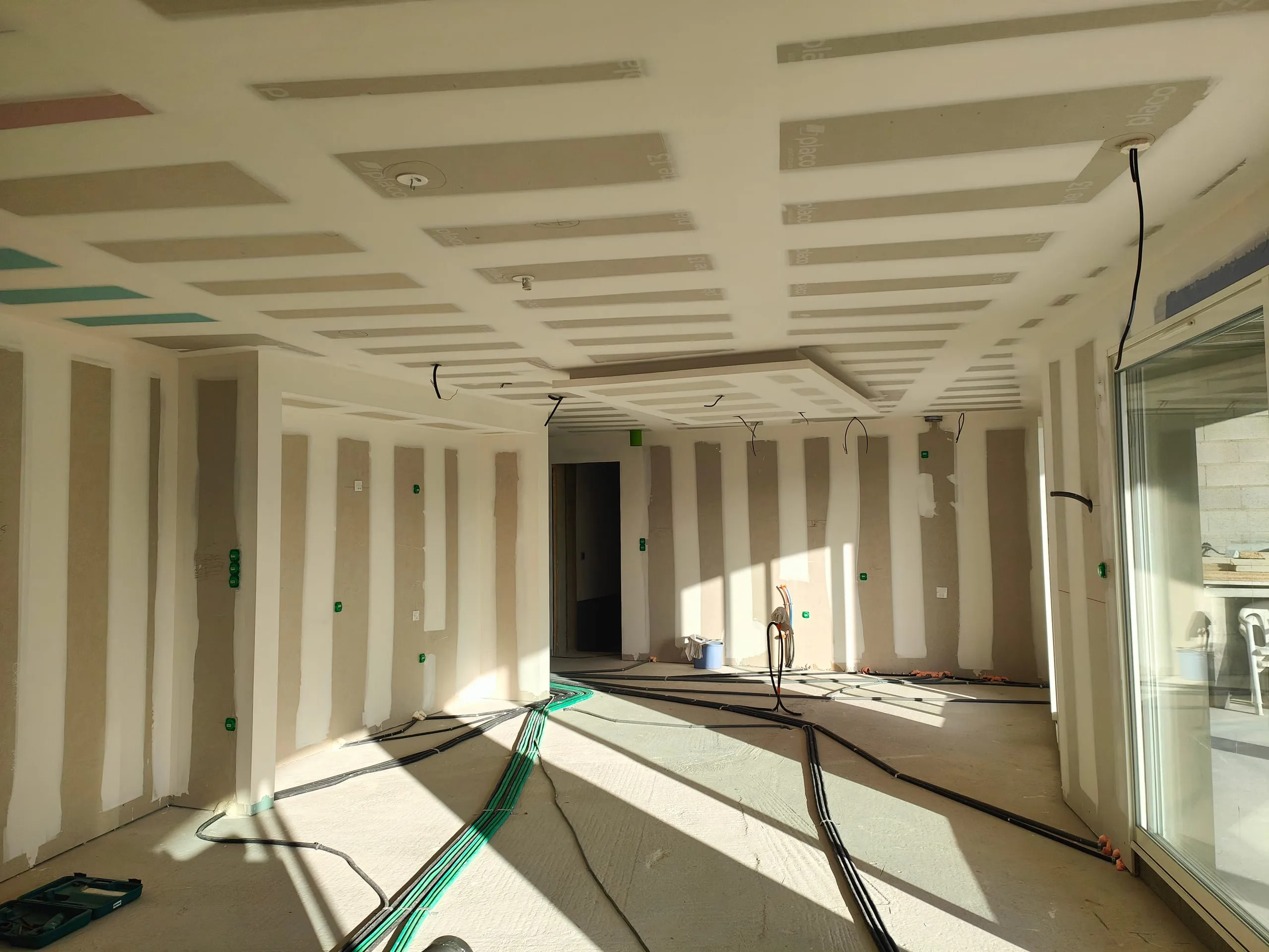 Pose de plaques de plâtre au plafond et sur les murs dans une pièce en cours de rénovation.