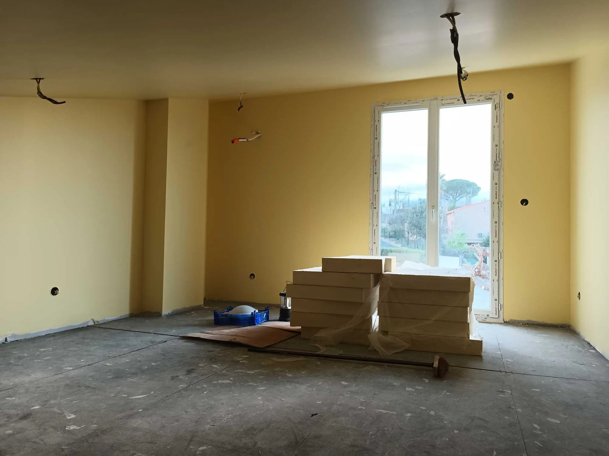 Pièce intérieure en travaux avec matériaux de placo et réseaux électriques apparents.