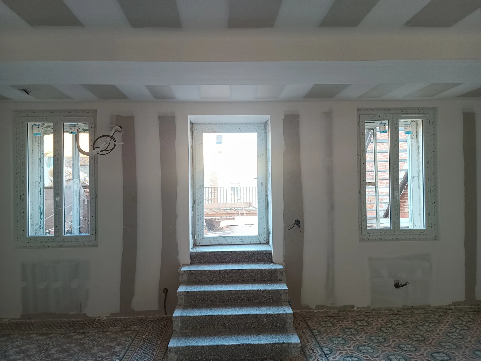 Mur de trois ouvertures avec porte-fenêtre, escalier en pierre, plafond en plaques et sol à motifs