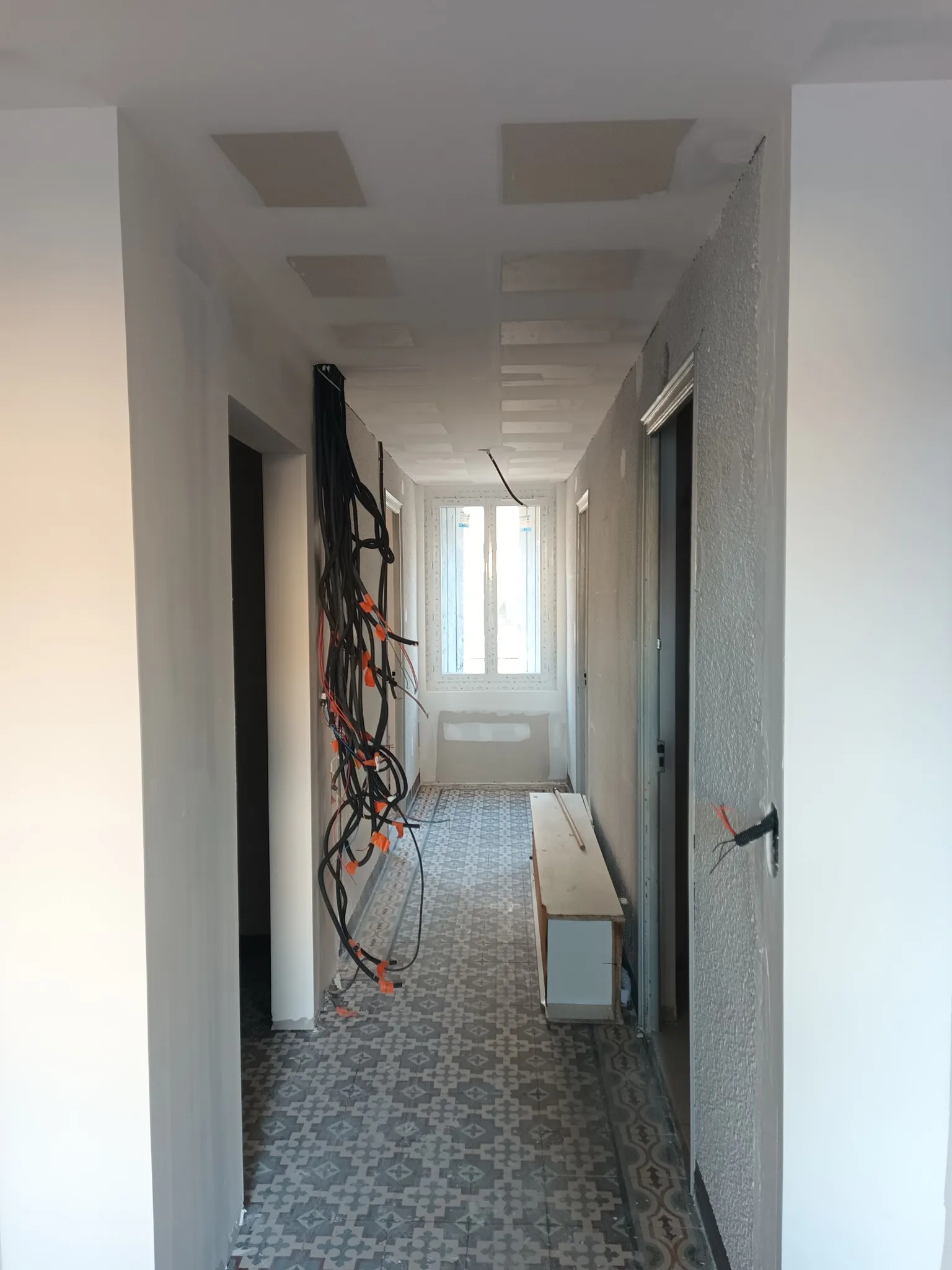 Couloir en rénovation avec plafond en plaques, cloisons blanches, fenêtre au fond et sol à motifs