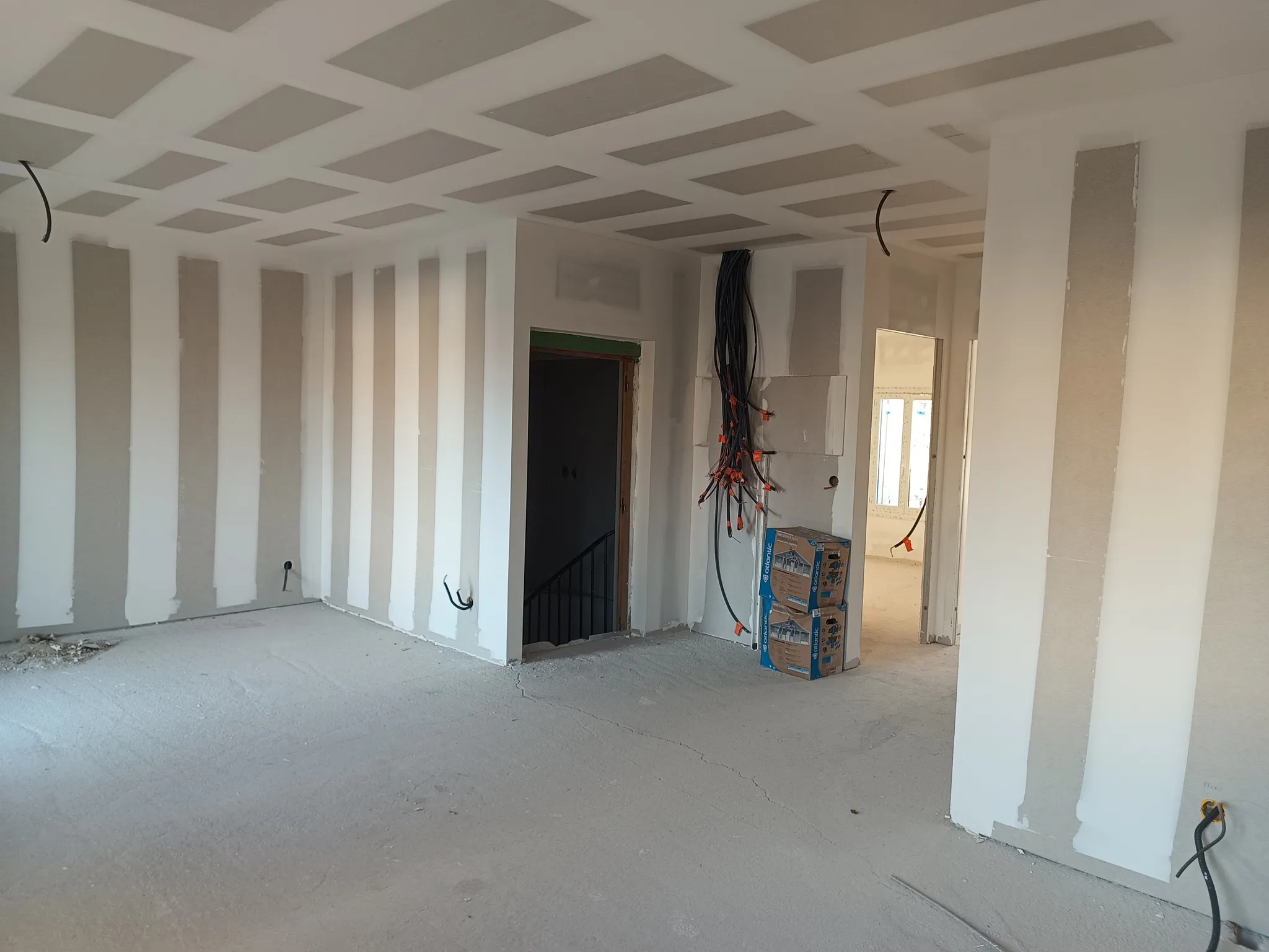 Pièce avec plafond en plaques de plâtre, cloisons montées, encadrement de porte et câbles regroupés